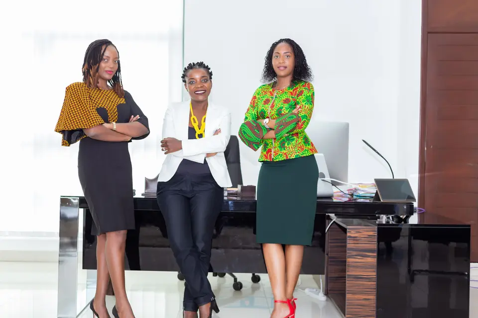 Three African businesswomen smiling together in a bright office.
