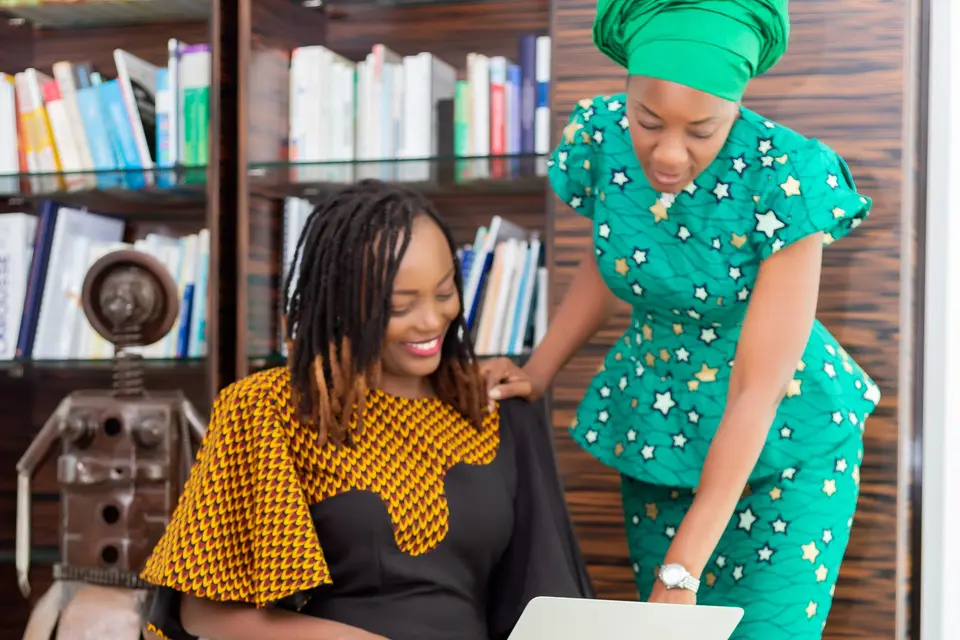 Two African women in Ankara dress working together on a laptop.