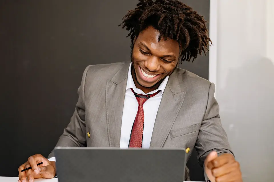 A smiling man in a suit working at a laptop.