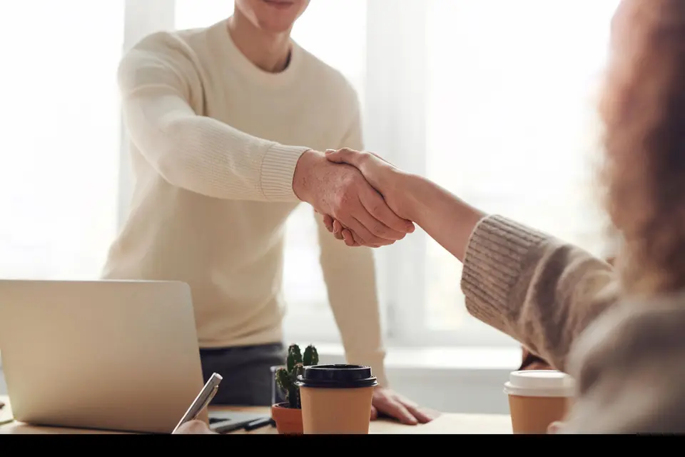 Two people shaking hands over a meeting table.