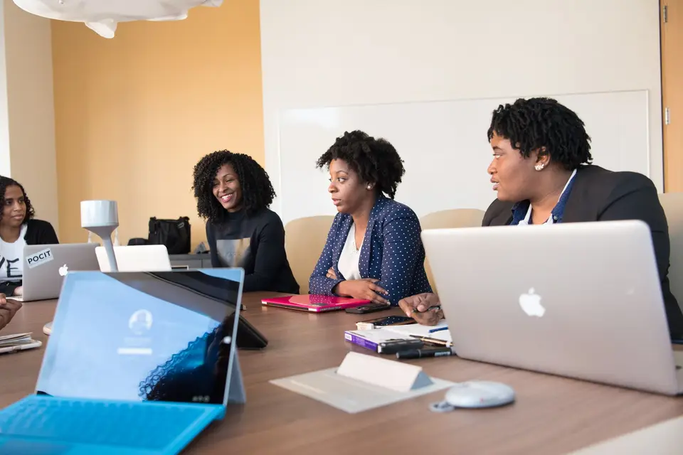 Three women sitting at a table with MacBook laptops.