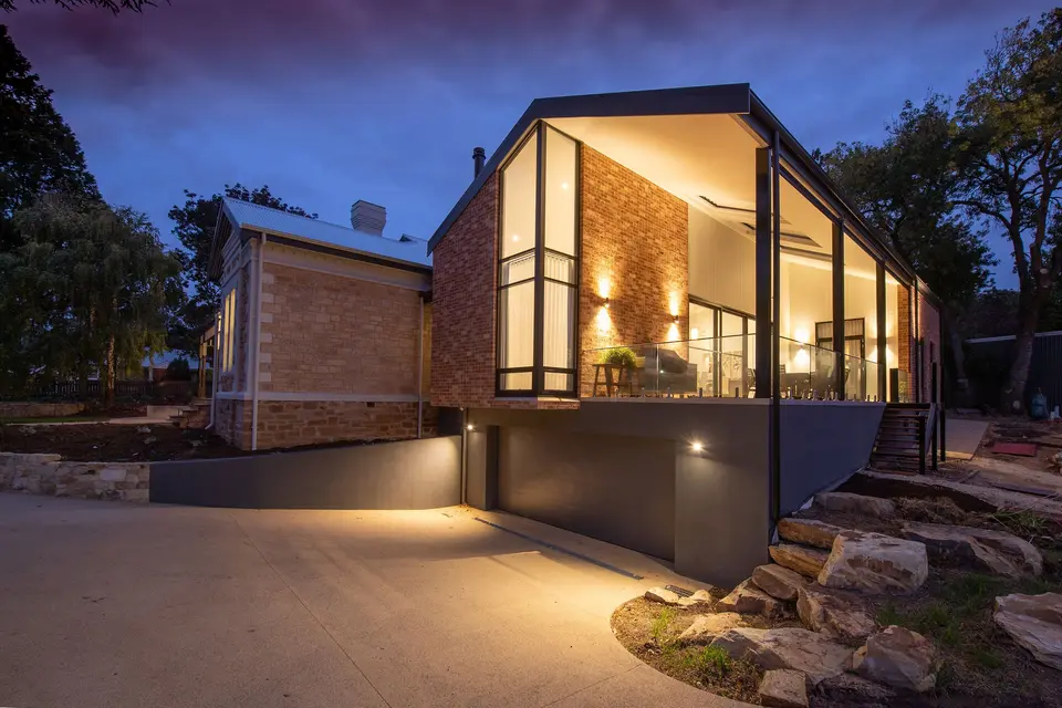 A modern brick house with warm interior lights at dusk, standing above a driveway.